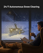 Autonomous Snow Blower Module with bright lights clearing snow outside, viewed from a cozy interior where a man reads.